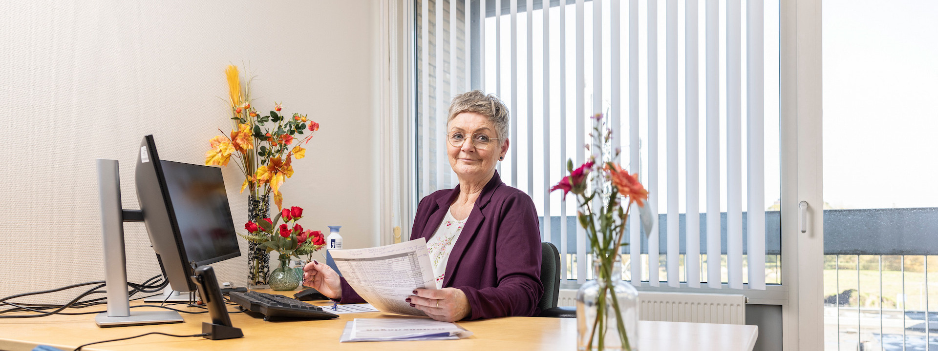 Vrouw werkt aan een bureau in een kantoor met bloemen op tafel.