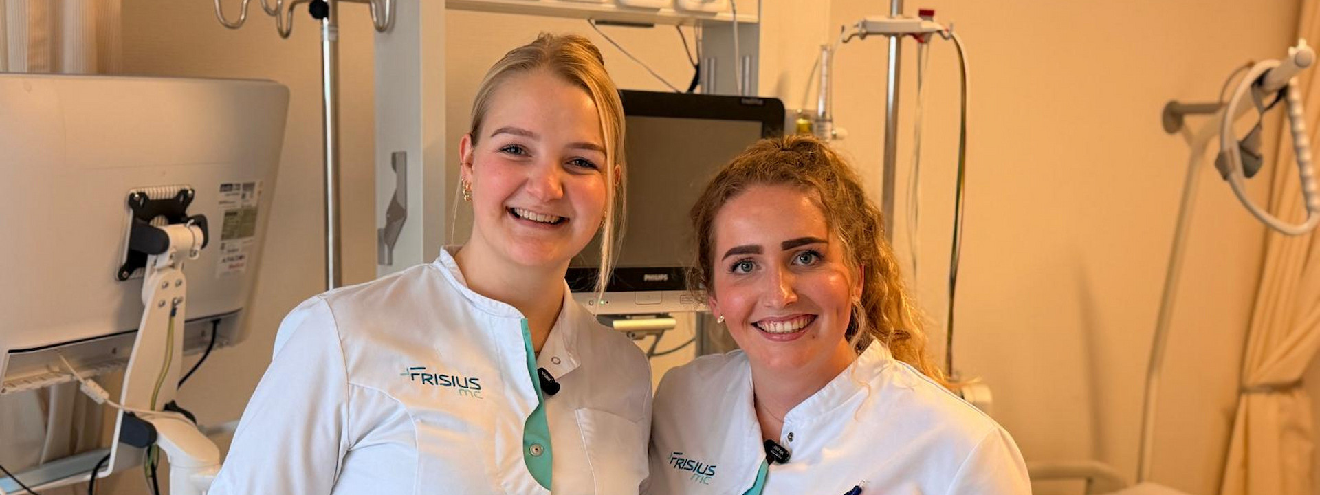 Twee verpleegkundigen glimlachen in een ziekenhuisomgeving.