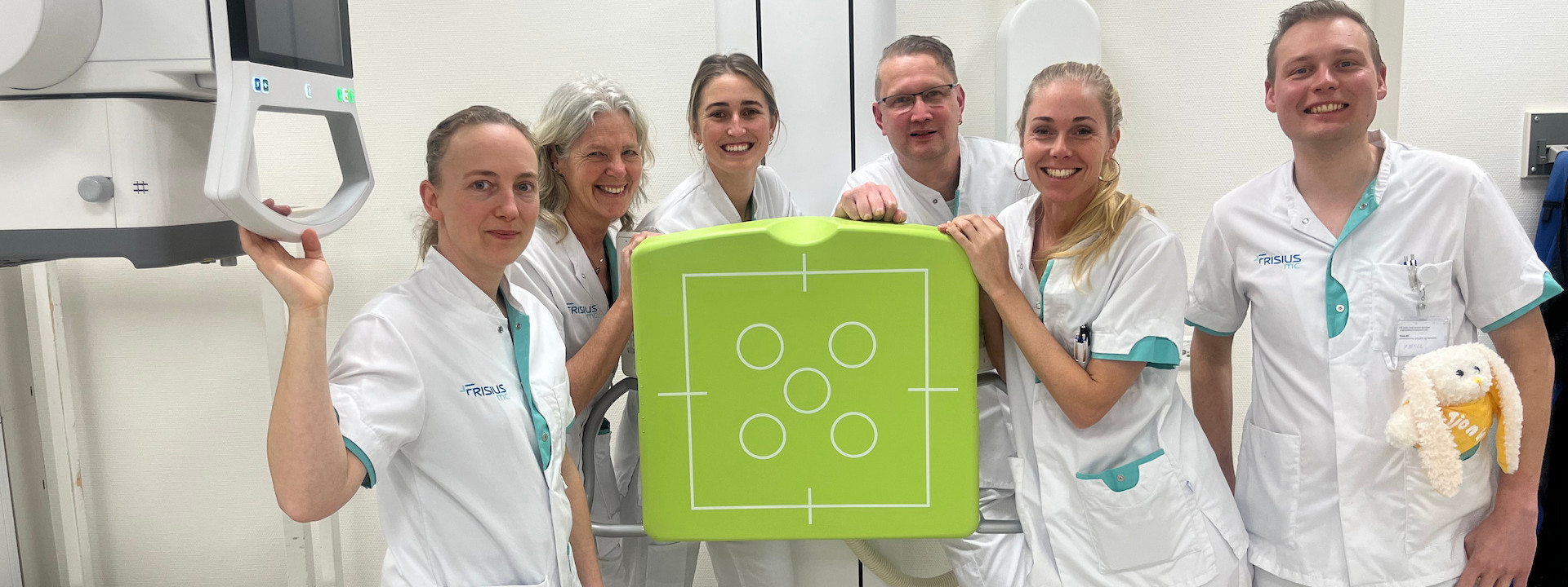 Medewerkers in een medische omgeving poseren met een groen rontgenbord.